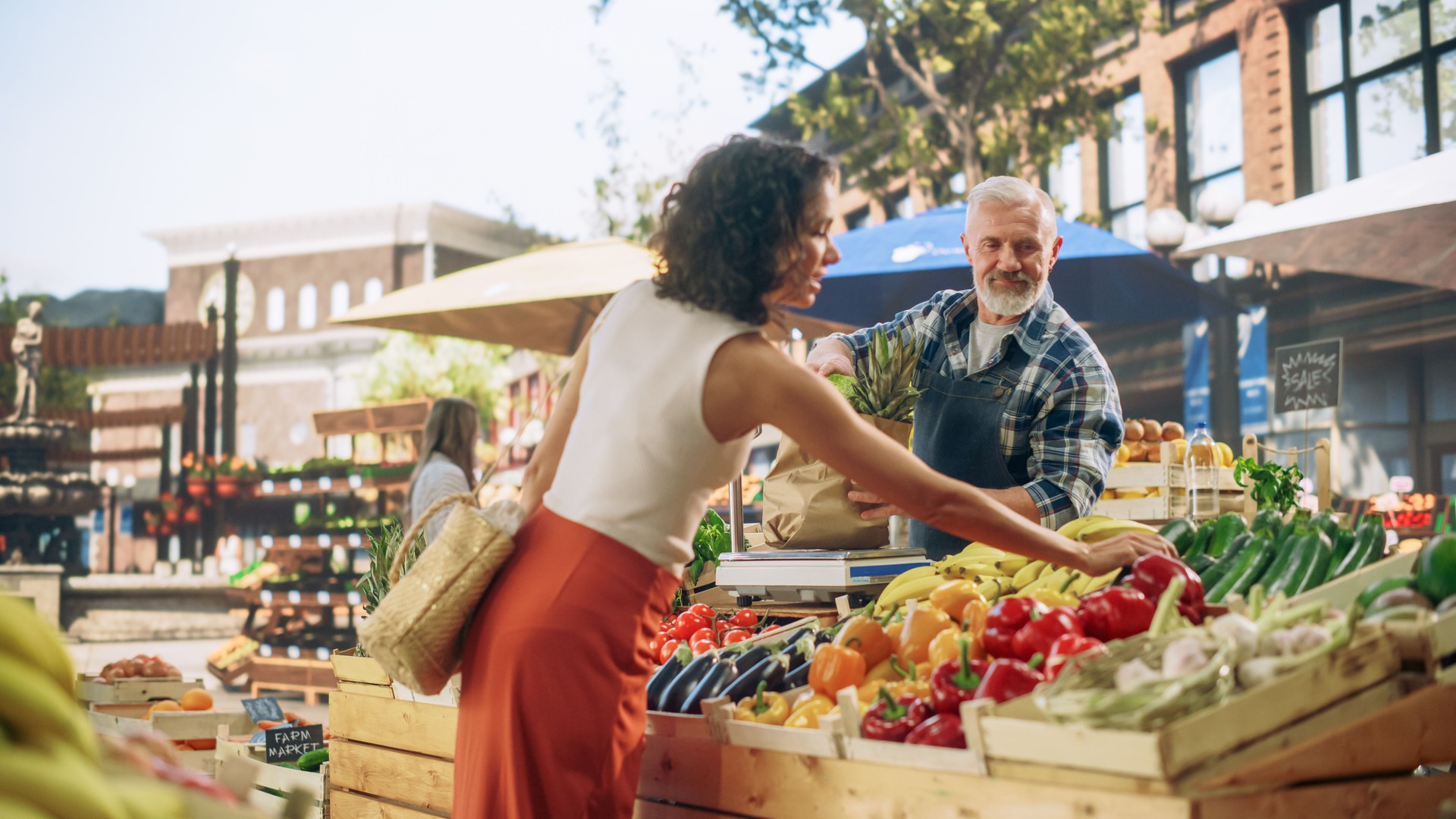 Cheerful Street Vendor Running a Small Farm Market Business, Selling Sustainable Fruits and Vegetables. Happy Middle Aged Man Filling a Recycled Paper Shopping Bag with Local Natural Food